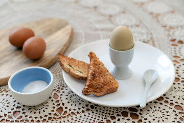 Tasty boiled egg in a cup with crunchy toasted bread for breakfast. Healthy meal on the kitchen table.