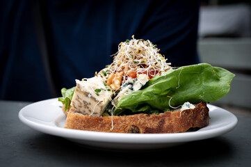A delicious cheese sandwhich topped with walnuts, marmelade, and vegetables