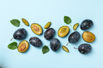 Fresh plums and leaves on blue background, top view