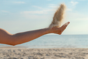 Close up of sand pouring from the hand on the beach on a sunny summer day. Playing with sand on vacation.