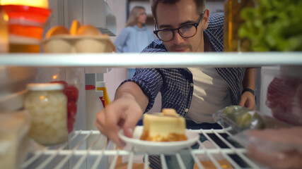 Hungry man looking for a snack in fridge taking piece of cake