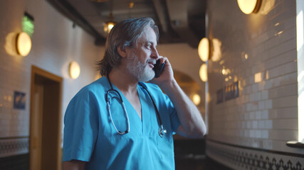 Mature male doctor talking on mobile phone in hospital corridor
