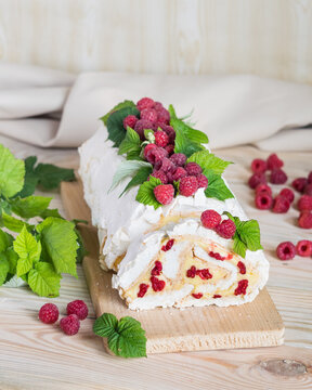Meringue roll cake with cream and fresh raspberries. Roulade, summer dessert. Selective focus, vertical orientation.