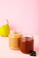 Glass jars with nutrient baby food on pink background