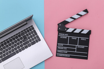 Fototapeta na wymiar Movie clapper board with laptop on a blue-pink pastel background. Filmmaking, Movie production, Entertainment industry. Top view