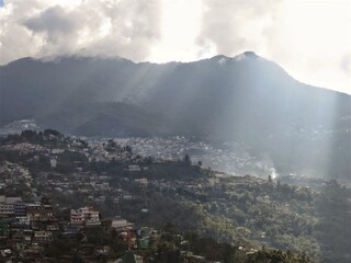 A landscape of the city of Kohima in Nagaland in Northeast India with sun light shafts falling from the cloudy sky on the surrounding hills.