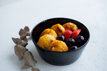 Syrniki cottage cheese fritters with summer berries on black plate, wooden table background. Russian sweet breakfast cheese.