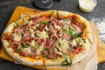 Delicious homemade pizza on a wooden table.Homemade pizza on a wooden plate on a dark background. Sprinkled flour, sauce and knife. 