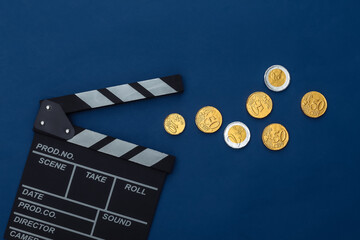 Movie clapper board and coins on classic blue background. Cinema fees. Filmmaking, Movie...