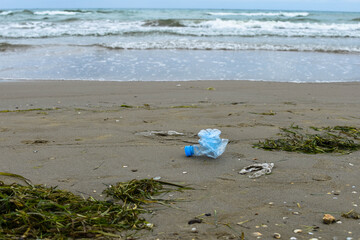 Seaweed, plastic bottle and bags in the sand on the beach. Environmental pollution. Plastic recycling