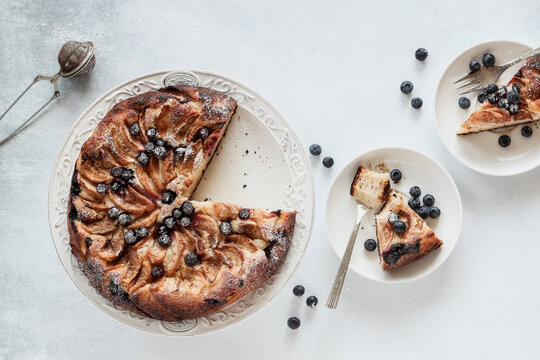 Sliced apple cake with blueberries served on a white table, shot from above