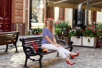 Young beautiful woman sits on a bench in the streets of the old city. The woman has a red handbag.