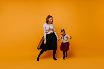 Full-length photo of dancing mom and little daughters. A young lady and a little girl are having fun in New Year's sweaters and elegant fluffy skirts.