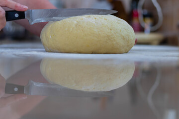 Old lady chef is cutting homemade fresh dough with knife, with reflection on the counter top.