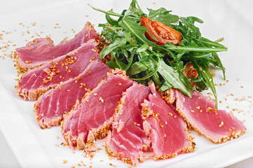 Sliced tuna fish grill with sesame seeds, tomatoes and arugula