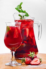 Wineglass of strawberry drink with fresh berries, ice, raspberry and mint leaves in jug