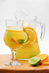 Wineglass of orange drink with fresh citrus fruits, ice, lime and mint leaves in jug
