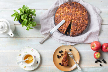 An apple pie next to a tea set on a light wooden board