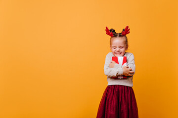 Little cute girl in a red skirt and a New Year's sweater tightly holding her New Year's gift