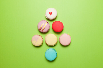 Colorful macarons or macaroons on a green background lined up in the shape of a small christmas tree, top view, copy space. Merry Christmas card concept for greeting