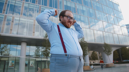 Portrait of overweight excited businessman doing winner gesture standing outdoors on street