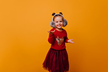 little girl is dancing incendiary dance in a bright, beautiful sweater with Christmas shiny deer. Baby in gray headphones on isolated background