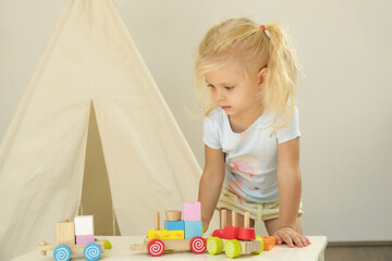 Toddler girl playing with wooden train made from wooden blocks - educational toys for preschool and kindergarten child. 