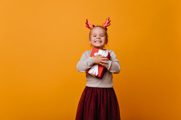 Little cute girl in a red skirt and a New Year's sweater tightly holding her New Year's gift