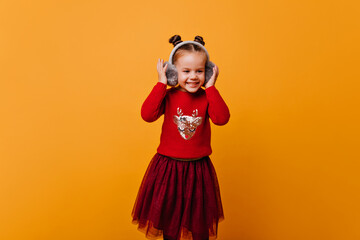 little girls in red New Year's sweater with Christmas deer and and in black fashionable skirt nicely smiling and holding on fur winter headphones
