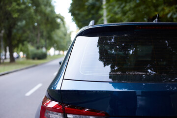 Back window of blue car parked on the street in summer sunny day, rear view. Mock-up for sticker or...