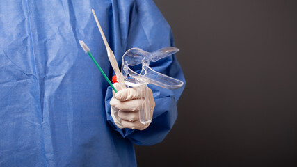 A female doctor is a gynecologist in a blue robe. Gynecological accessories, venus mirror, brush. Grey background, empty space for text.