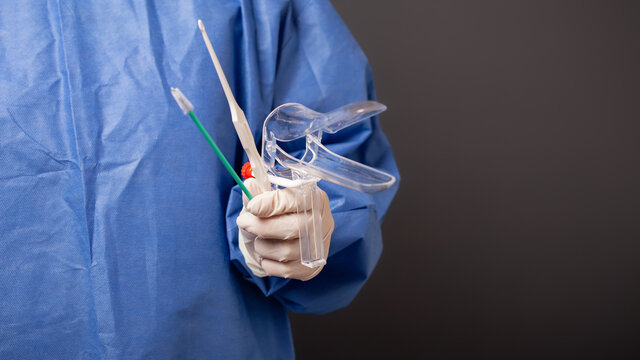 A female doctor is a gynecologist in a blue robe. Gynecological accessories, venus mirror, brush. Grey background, empty space for text.