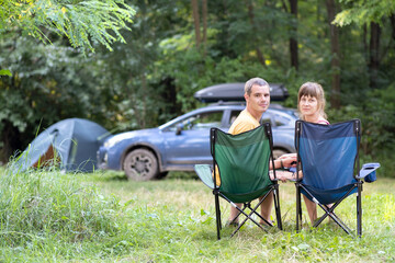 Happy couple sitting on chairs at campsite relaxing together. Travel, camping and vacations concept.