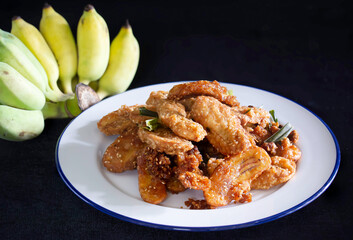 Fried banana mix sesame and pandan leaf for aroma (Thai called Kluay Thod) in white dish and Banana on black cloth background Thai snack