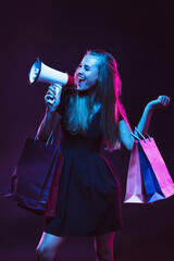 Shouting with shopping bags for sales. Portrait of young woman in neon light on dark backgound. The...