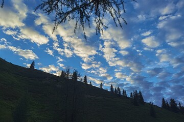sunset on the mountains with blue sky, clouds and tree silhouettes
