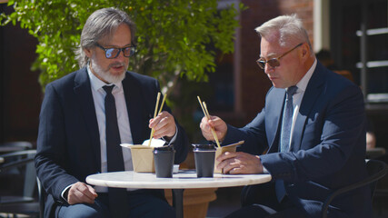 Two mature businessmen having lunch outdoors discussing startup project
