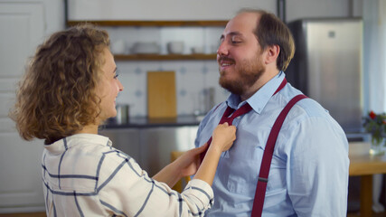 Beautiful wife tying red necktie to her overweight husband at home