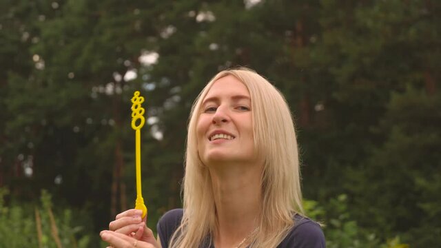 A young woman blows bubbles in nature. A happy young blonde is walking in the Park and blowing soap bubbles on a Sunny day.