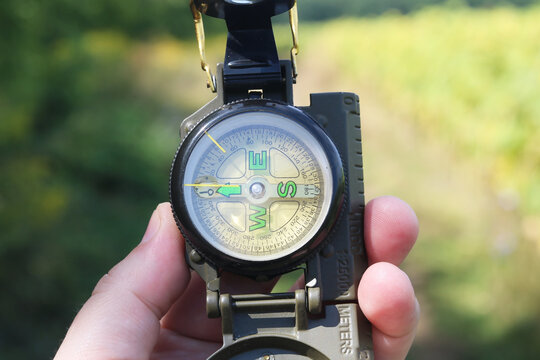 Old classic navigation compass in hand on natural background as symbol of tourism with compass, travel with compass and outdoor activities with compass