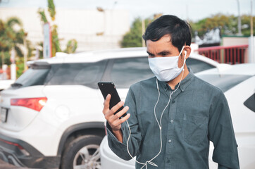 Fototapeta na wymiar Man wearing a mask stands using a smartphone, a new normal social lifestyle after lockdown the corona virus.
