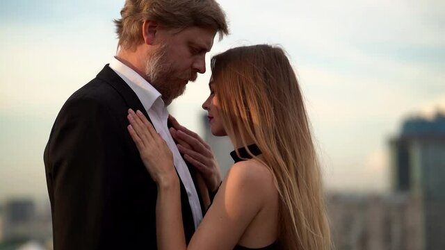 A couple are embracing on the street, against the background of the city's beautiful buildings and sky. They are located on a street, say goodbye to each other and he takes the hand of another girl.