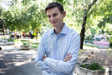 Portrait of young smiled man in a blue shirt on the city with a trees on the background. The man in conversation, listens and speaks. American or European appearance