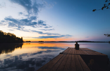 Person sitting on dock at sunset