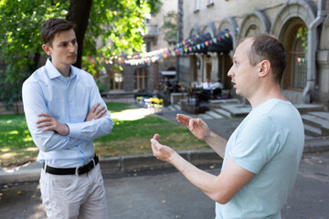 Two men talk nicely on the street. One American and one European. Two colleagues met in the city. Acquaintance. surprised face. Cafe and green trees on the background.