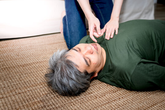 Woman use their fingers, check the breath of a middle aged Asian man lying on the floor unconscious, Before making the first battle, to health care and CPR concept.
