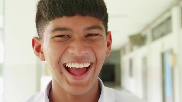 Laughing male Asian high school bang hair and tan skin student in white uniform.