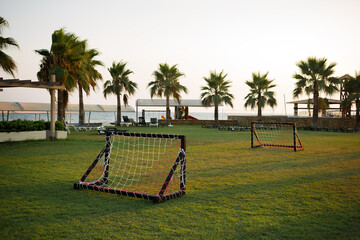 Empty small kids soccer field on vacation at sunset with beautiful green grass. Palm trees in the background. Football. Leisure. Active games. sport. Relax. Weekend. Bright setting sun. Resort