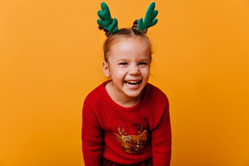 beautiful, cheerful little girl of 4-6 years old in red warm Christmas sweater and glittering blue...