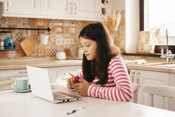 Teenage girl watching video tutorial on laptop in kitchen, distance learning, online education, home learning concept